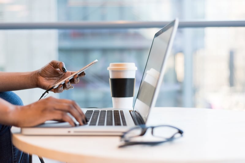 Hände bedienen ein Laptop, das auf einem Tisch neben einem Kaffeebecher steht