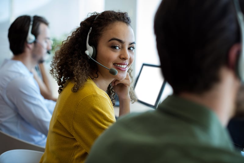 Eine lächelnde Frau mit Headset sitzt neben anderen Personen