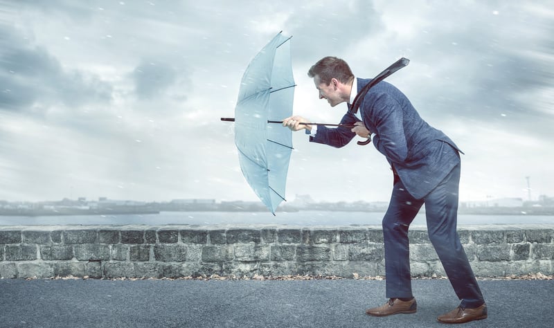 Ein Business Man stemmt bei Regenfall seinen Regenschirm gegen den Wind