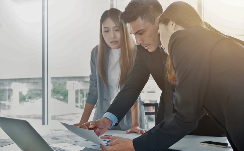Ein Business Man und zwei Business Women schmieden Pläne an einem Schreibtisch