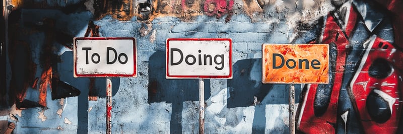 Drei Schilder Schilder vor einer Graffiti-Wand, auf denen steht: To Do, Doing, Done.