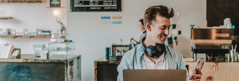 Mann mit Laptop und Headset schaut auf sein Smartphone