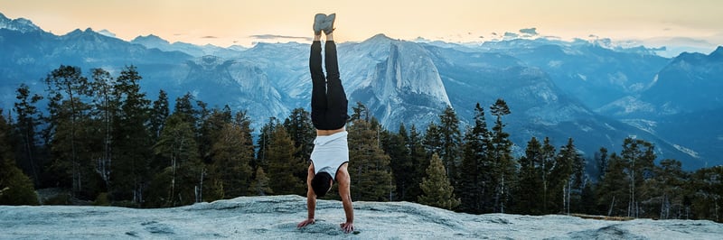 Ein Mann macht einen Handstand auf einem Hügel vor Bergpanorama