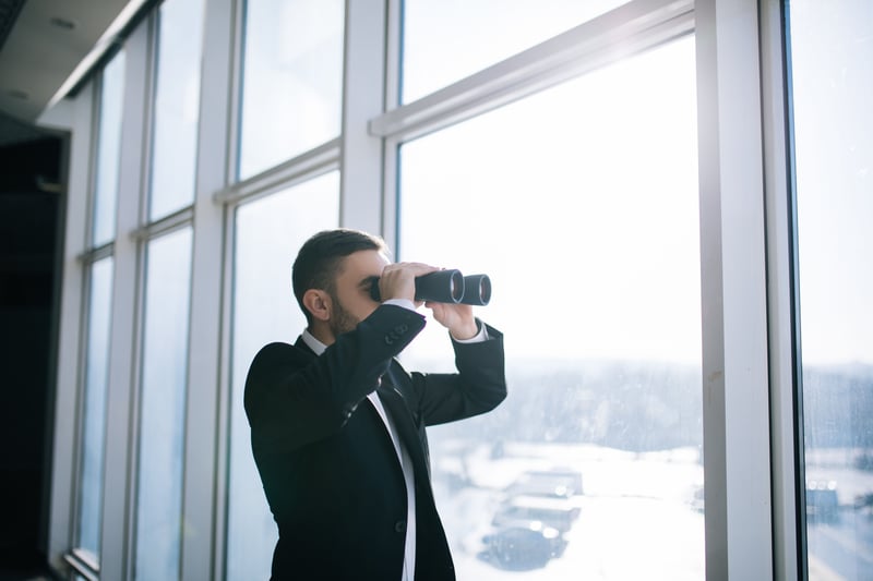 Mann schaut mit Fernglas aus Fenster